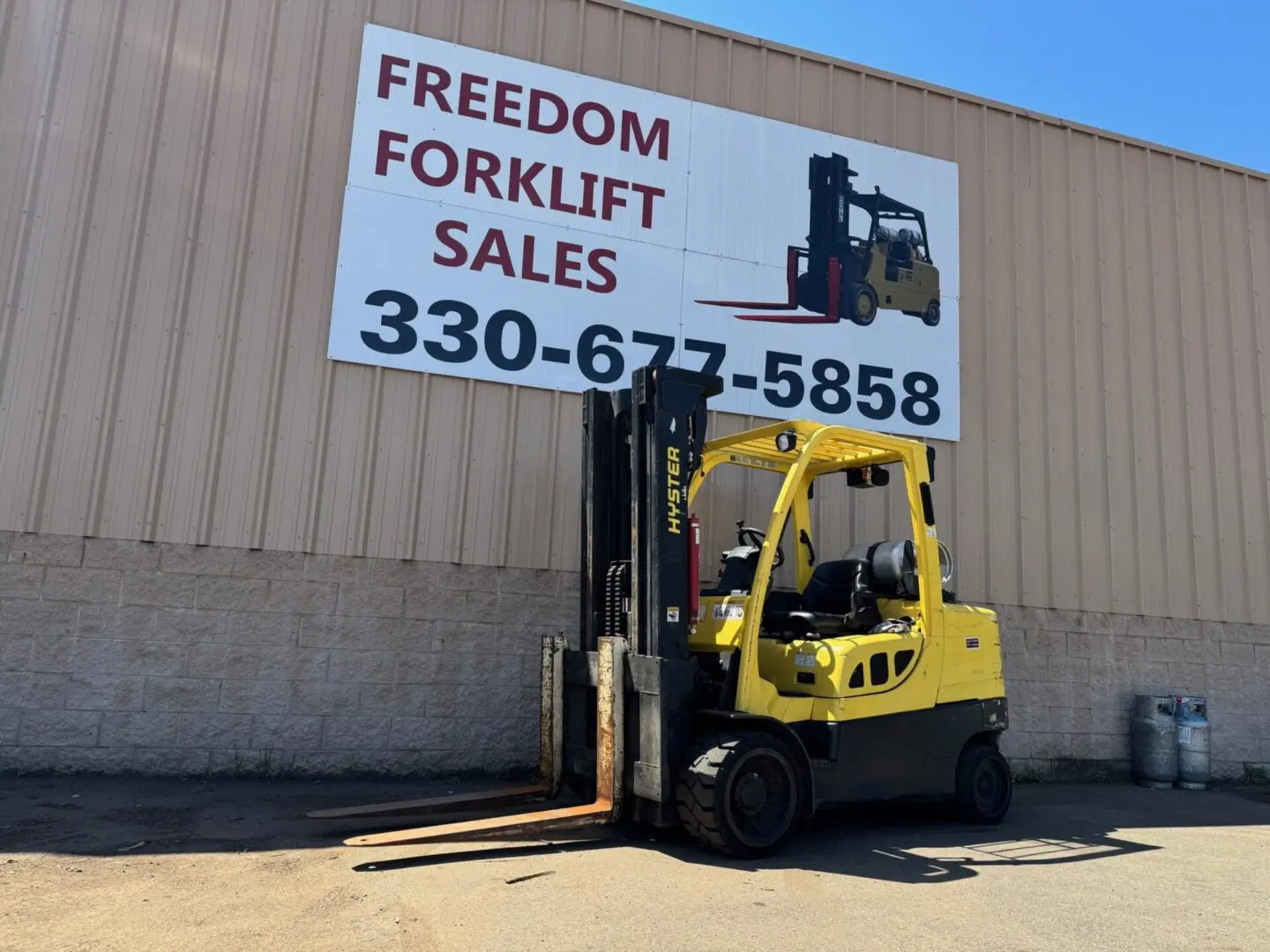 Yellow forklift parked under sales sign.