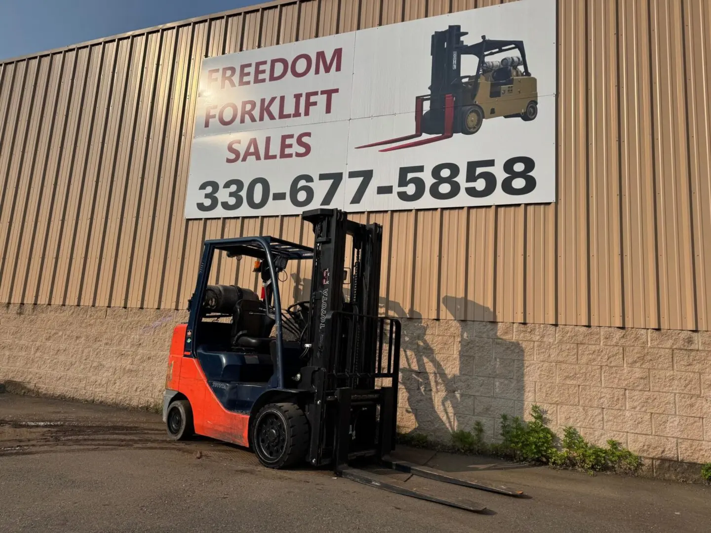 Forklift parked near sales sign, sunny day.