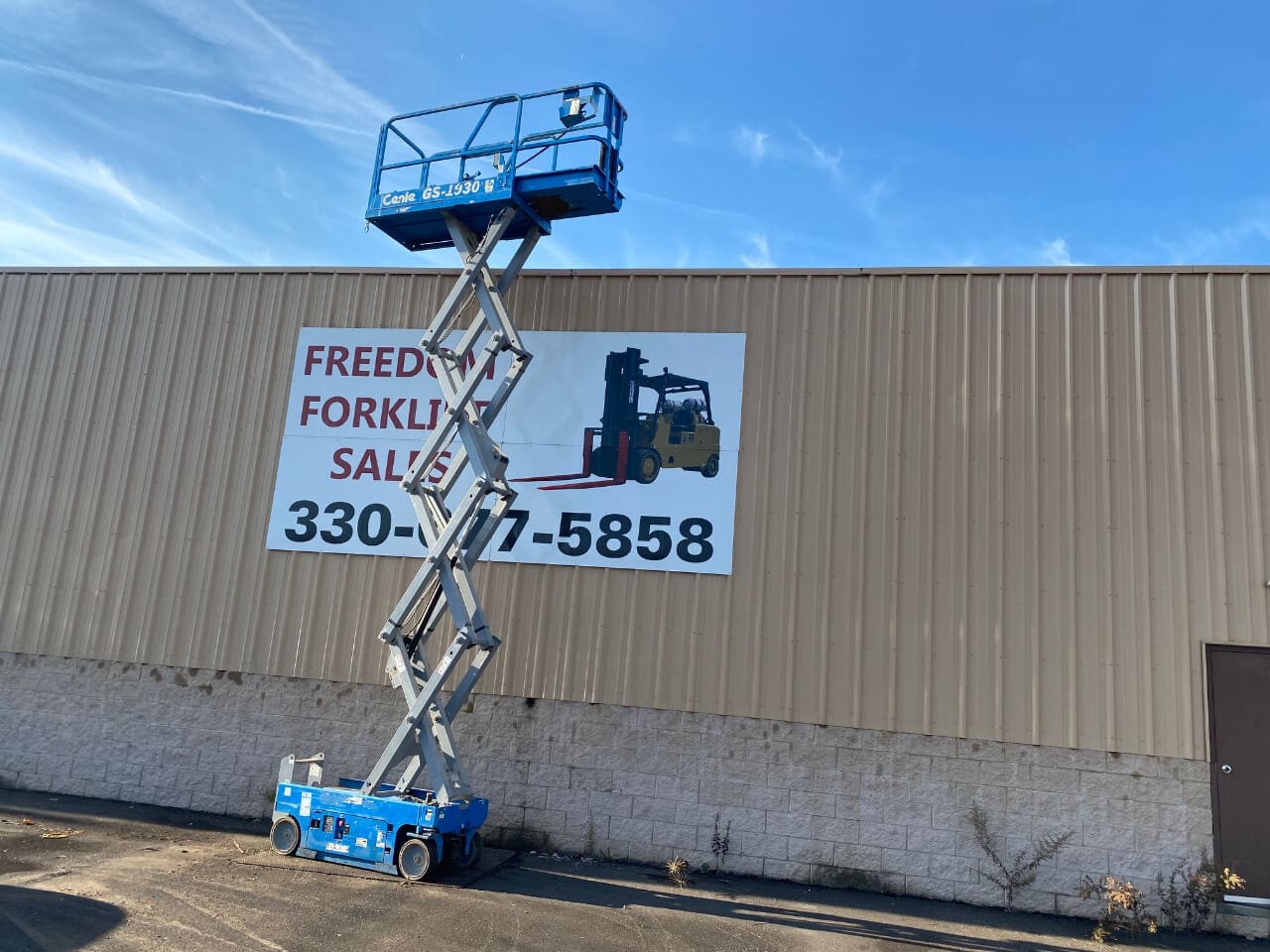 A man on a scissor lift in front of a building.