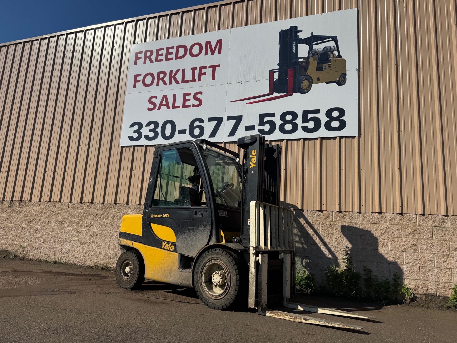 Forklift parked below sales sign outdoors.